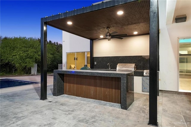 patio terrace at dusk with area for grilling, sink, and ceiling fan