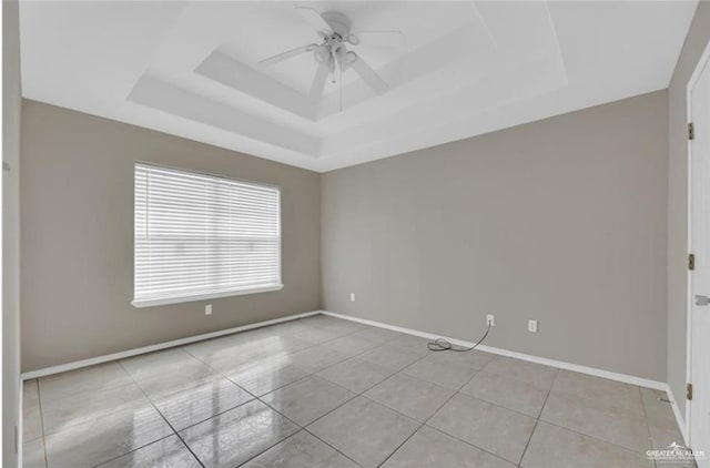 tiled empty room with a tray ceiling, a ceiling fan, and baseboards