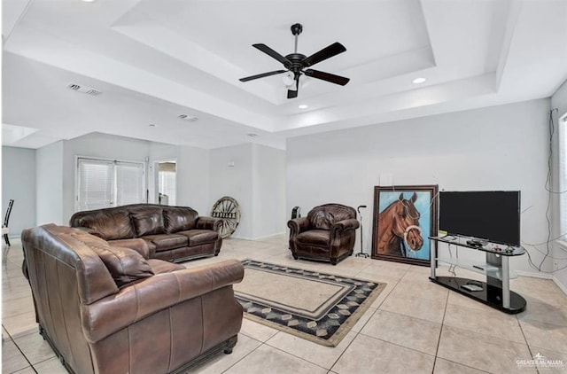 living room featuring visible vents, a ceiling fan, a tray ceiling, light tile patterned flooring, and baseboards