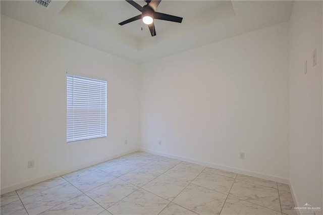 unfurnished room with marble finish floor, a raised ceiling, and baseboards