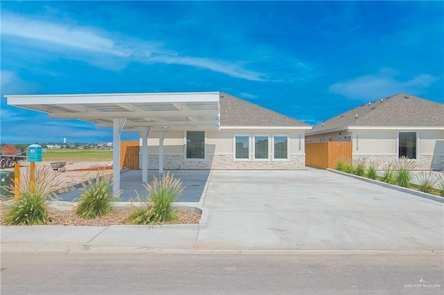 view of front of property featuring stucco siding, a shingled roof, fence, stone siding, and driveway