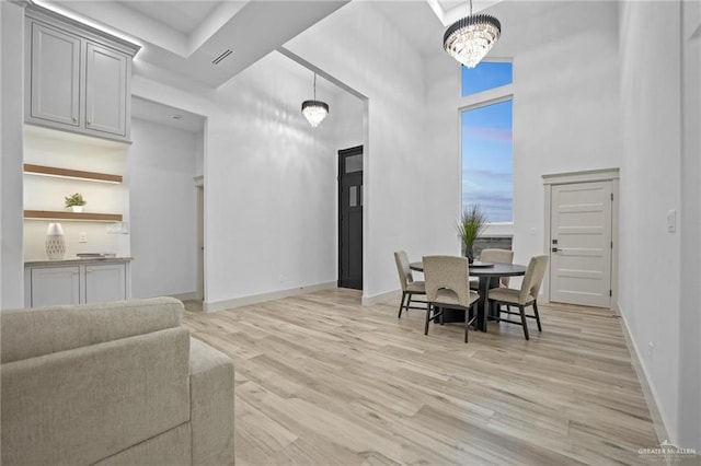 dining area featuring visible vents, a towering ceiling, an inviting chandelier, light wood-style floors, and baseboards