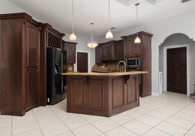 kitchen featuring arched walkways, decorative light fixtures, stainless steel microwave, black refrigerator with ice dispenser, and dark brown cabinets