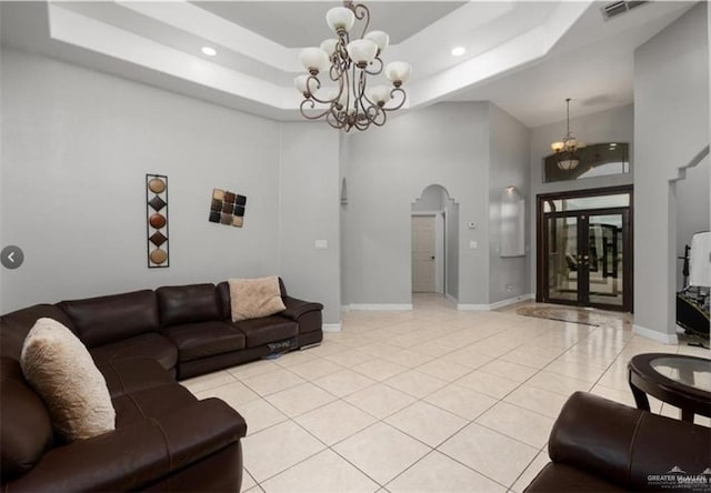 living area with light tile patterned floors, visible vents, arched walkways, a raised ceiling, and a chandelier