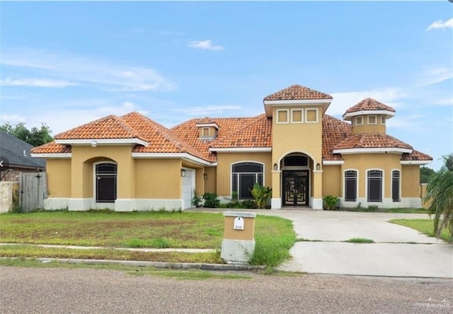 mediterranean / spanish-style home featuring driveway, a front lawn, a tiled roof, and stucco siding