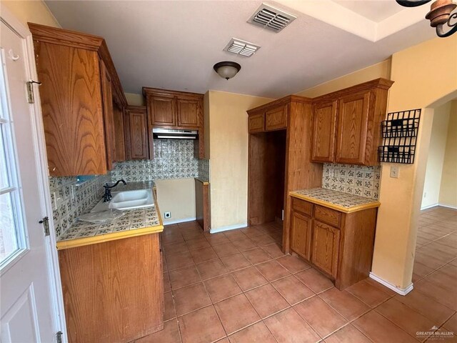 1008 Ivory Ave, Rio Grande City, TX 78582 - kitchen with a sink, brown cabinetry, under cabinet range hood, tasteful backsplash, and light tile patterned flooring