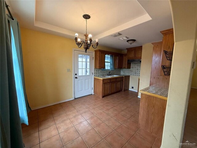 1008 Ivory Ave, Rio Grande City, TX 78582 - kitchen with a raised ceiling, tasteful backsplash, brown cabinets, and a chandelier