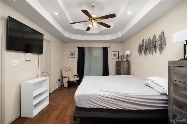 bedroom with ceiling fan, dark hardwood / wood-style floors, and a tray ceiling