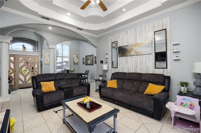 tiled living room featuring ceiling fan, a raised ceiling, ornate columns, and ornamental molding