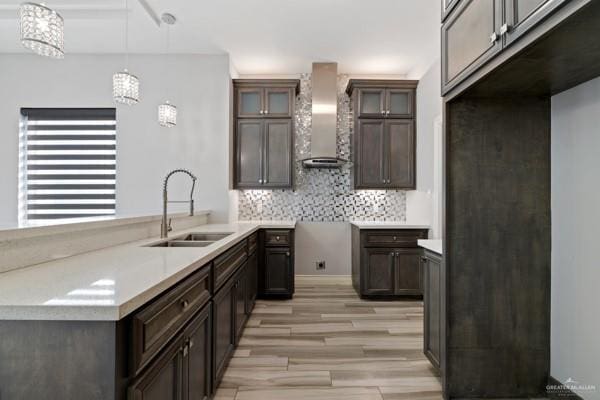 kitchen featuring backsplash, dark brown cabinets, sink, wall chimney range hood, and decorative light fixtures