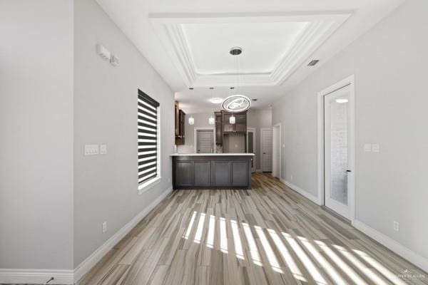 interior space with decorative light fixtures, light wood-type flooring, a tray ceiling, and dark brown cabinets