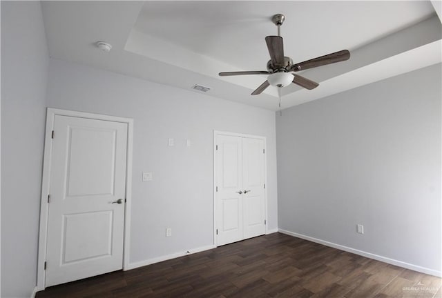 unfurnished bedroom featuring ceiling fan, a tray ceiling, and dark hardwood / wood-style floors