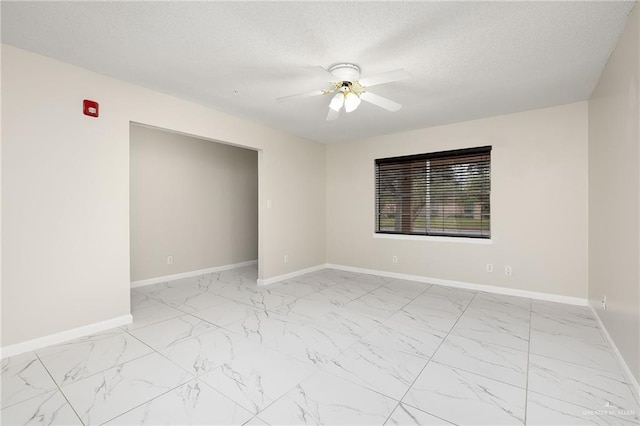 spare room featuring a ceiling fan, marble finish floor, a textured ceiling, and baseboards