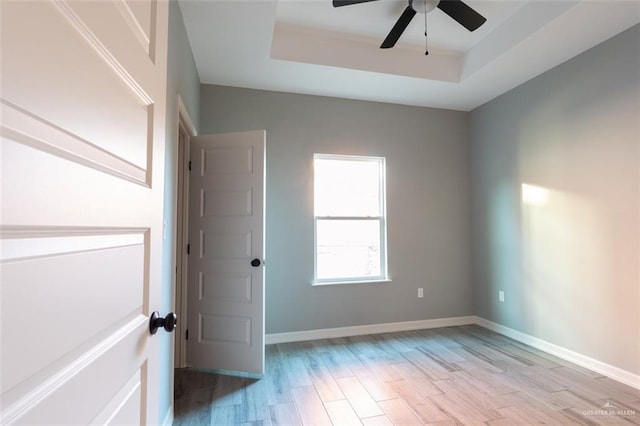 empty room featuring a raised ceiling, ceiling fan, and light hardwood / wood-style floors