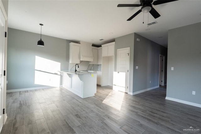 kitchen with pendant lighting, sink, premium range hood, a kitchen breakfast bar, and white cabinets