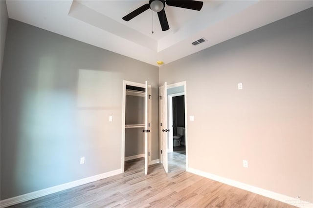 unfurnished bedroom featuring a raised ceiling, light wood-type flooring, ceiling fan, and a closet