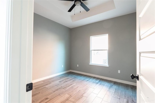 spare room with a tray ceiling, ceiling fan, and light wood-type flooring