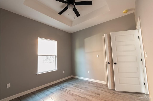 unfurnished room featuring a raised ceiling, light wood-type flooring, and ceiling fan