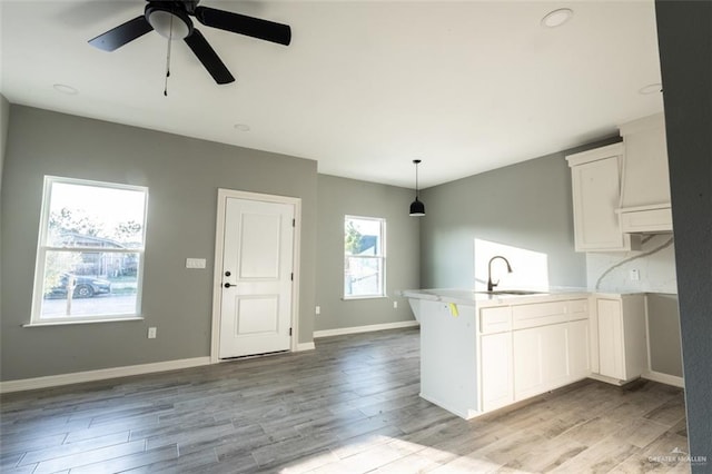 kitchen featuring decorative light fixtures, kitchen peninsula, sink, and white cabinets