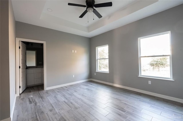 spare room featuring light hardwood / wood-style flooring, ceiling fan, and a tray ceiling