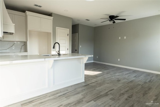 kitchen with sink, light hardwood / wood-style flooring, ceiling fan, white cabinetry, and tasteful backsplash