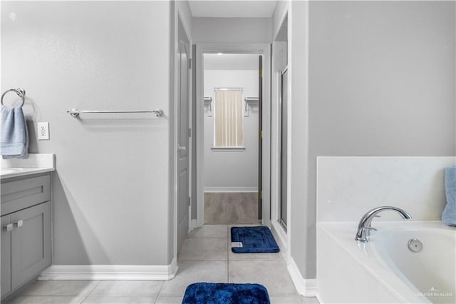 full bath featuring a garden tub, vanity, baseboards, tile patterned floors, and a stall shower