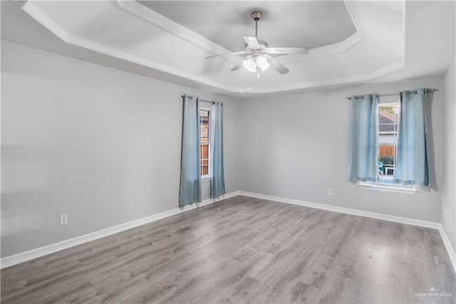 empty room featuring a ceiling fan, a tray ceiling, baseboards, and wood finished floors