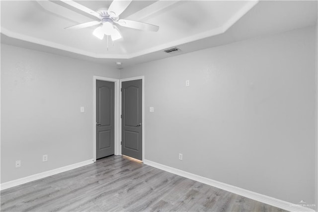 unfurnished room with light wood-style flooring, baseboards, and a tray ceiling