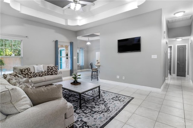 living area with light tile patterned floors, a tray ceiling, visible vents, and baseboards