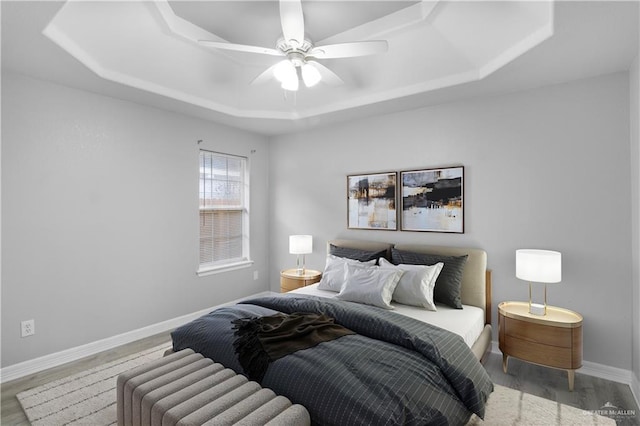 bedroom featuring a tray ceiling, wood finished floors, a ceiling fan, and baseboards