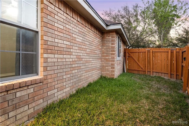 property exterior at dusk featuring a yard, fence, and brick siding