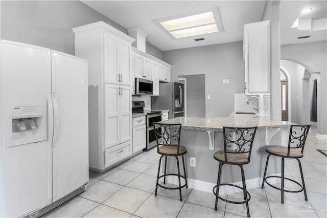 kitchen with arched walkways, appliances with stainless steel finishes, a breakfast bar area, a peninsula, and a sink