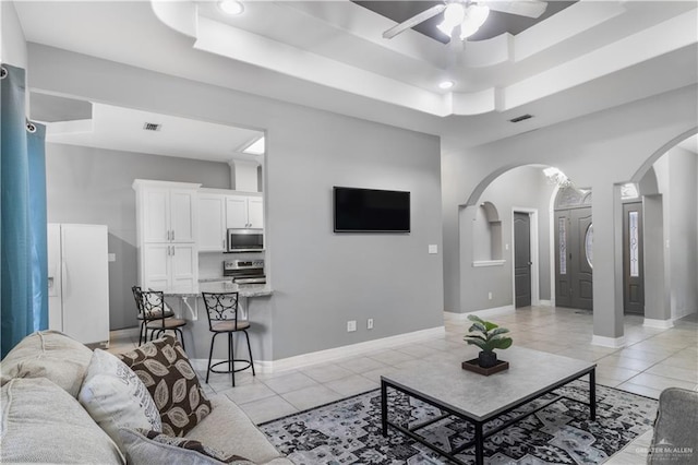 living room featuring arched walkways, light tile patterned flooring, a raised ceiling, and visible vents