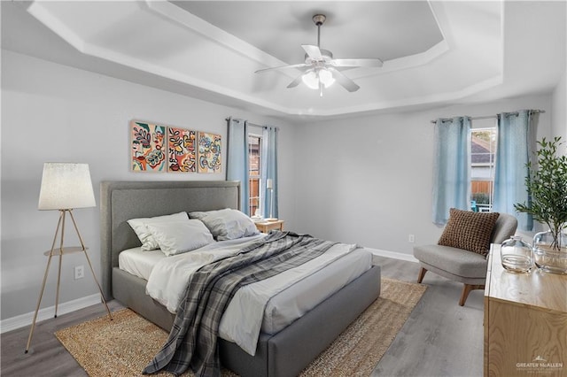 bedroom with a tray ceiling, baseboards, and wood finished floors