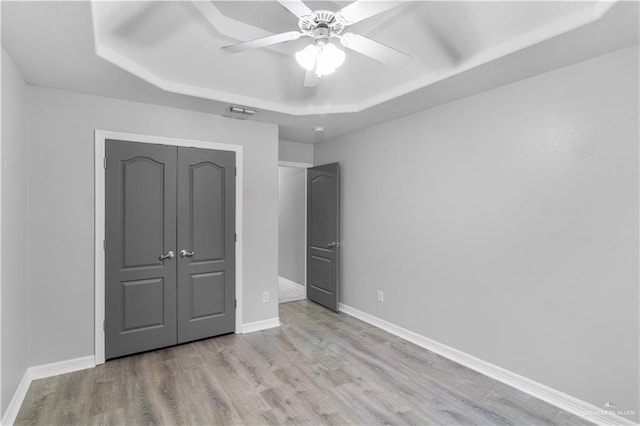 unfurnished bedroom featuring baseboards, visible vents, a tray ceiling, and wood finished floors