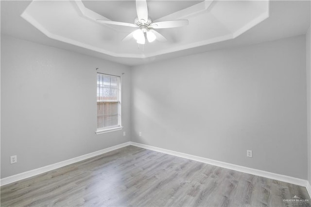 spare room with a tray ceiling, wood finished floors, a ceiling fan, and baseboards