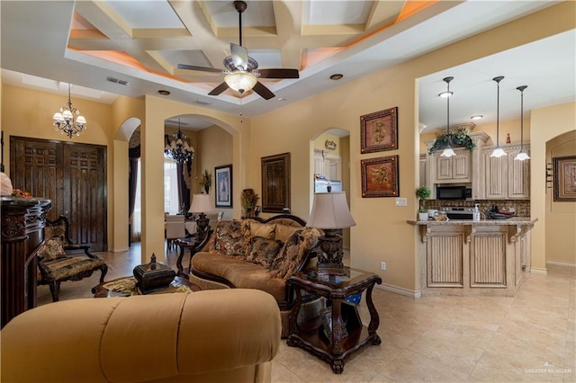 tiled living room with ceiling fan with notable chandelier, beam ceiling, and coffered ceiling