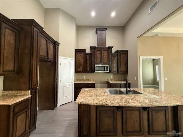 2315 N Ruby Dr, Edinburg, TX 78541 - kitchen featuring stainless steel microwave, a sink, a kitchen island with sink, dark brown cabinetry, and light stone counters