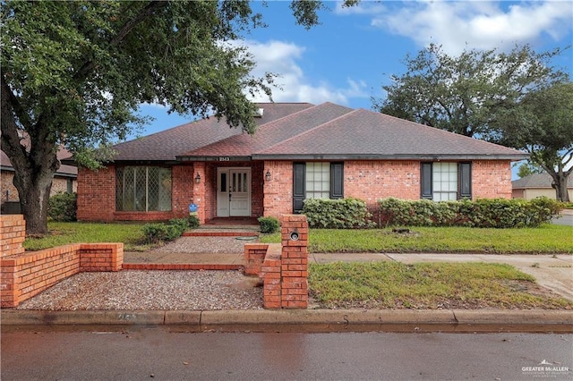 single story home with a shingled roof, a front yard, and brick siding