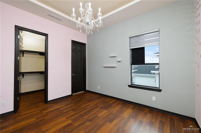 unfurnished bedroom featuring a notable chandelier, a walk in closet, a closet, and dark hardwood / wood-style floors