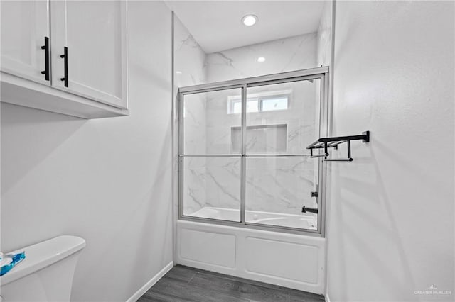 bathroom featuring hardwood / wood-style floors, enclosed tub / shower combo, and toilet