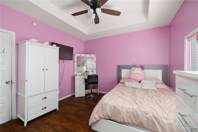 bedroom with dark wood-type flooring, ceiling fan, and a tray ceiling