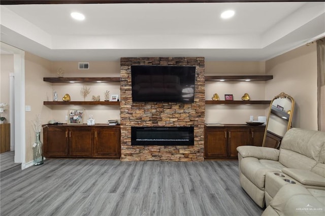 living room with a fireplace, a raised ceiling, and light wood-type flooring