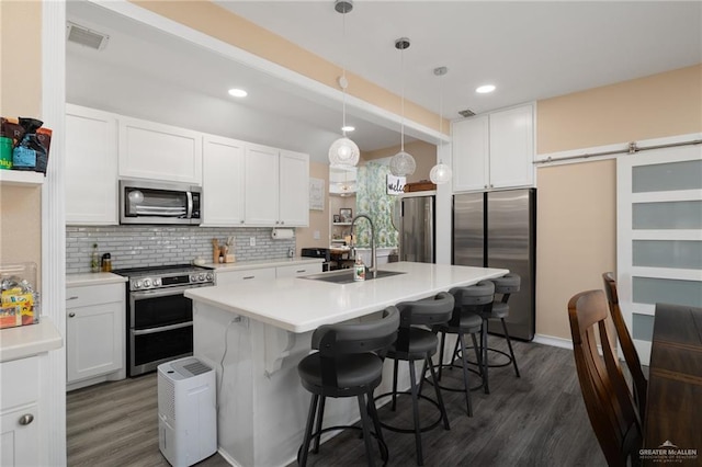 kitchen featuring appliances with stainless steel finishes, pendant lighting, sink, white cabinets, and a barn door