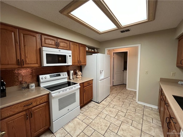 kitchen with decorative backsplash, light tile patterned floors, white appliances, and a textured ceiling