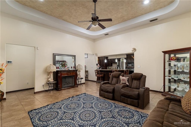 living room with a tray ceiling, a fireplace, a towering ceiling, and a ceiling fan