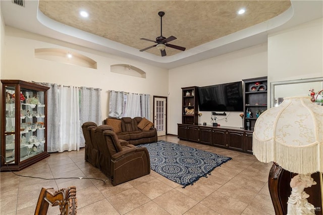 living area featuring a tray ceiling, ceiling fan, a towering ceiling, and light tile patterned floors