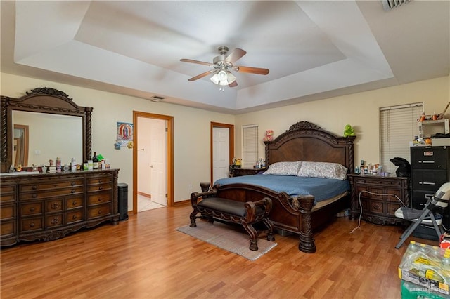 bedroom featuring light wood finished floors, visible vents, a tray ceiling, and ceiling fan