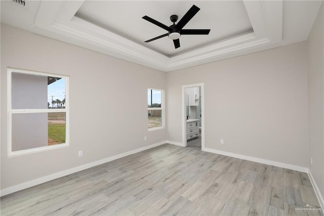 empty room with light wood-type flooring, baseboards, a tray ceiling, and ceiling fan