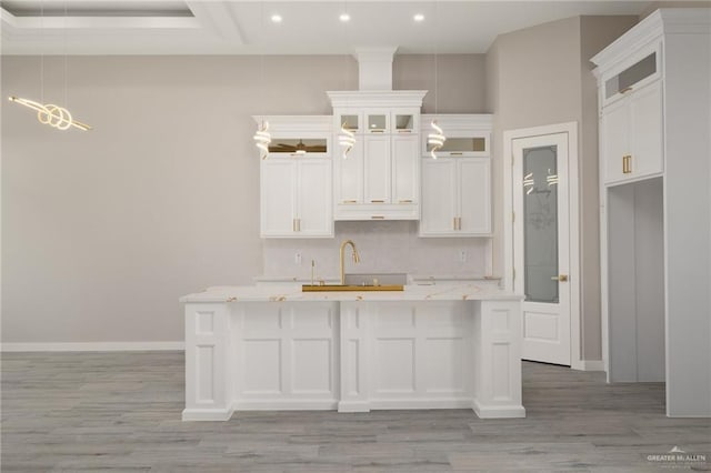 kitchen featuring a kitchen island with sink, a sink, white cabinetry, light countertops, and tasteful backsplash